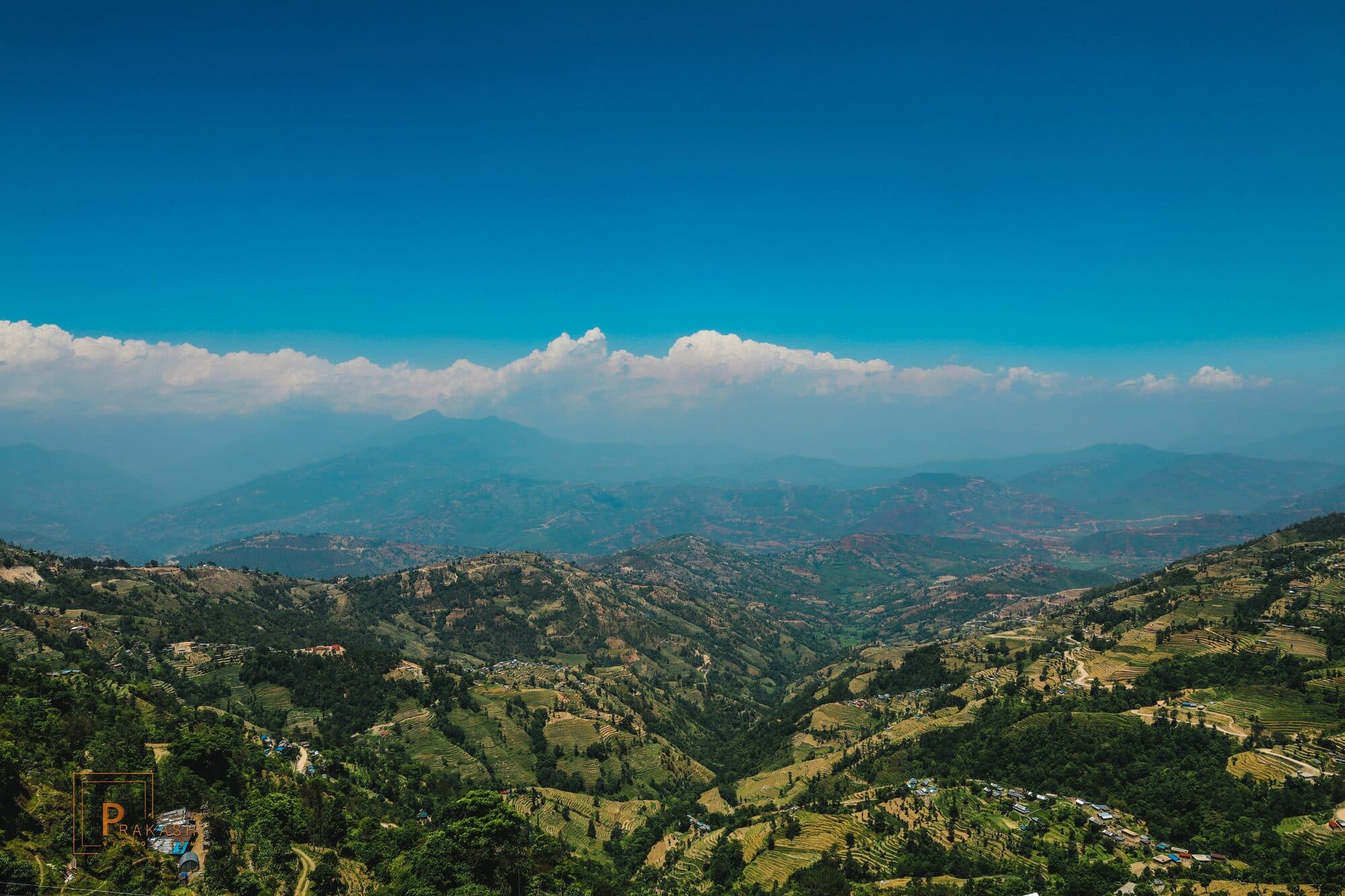 Terraced hills and hazy ridges near Kathmandu, under a band of cloud